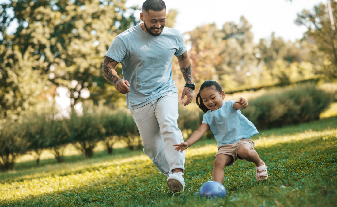Father and toddler playing soccer in field