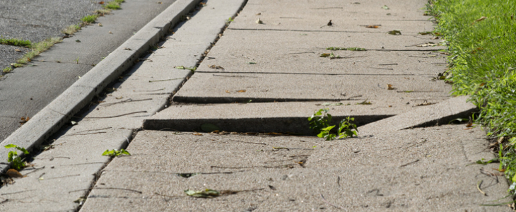 Uneven and cracked sidewalk on someone's property, representing premises liability