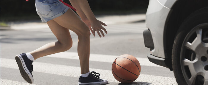 A girl runs into the street to get her ball as a car drives at her