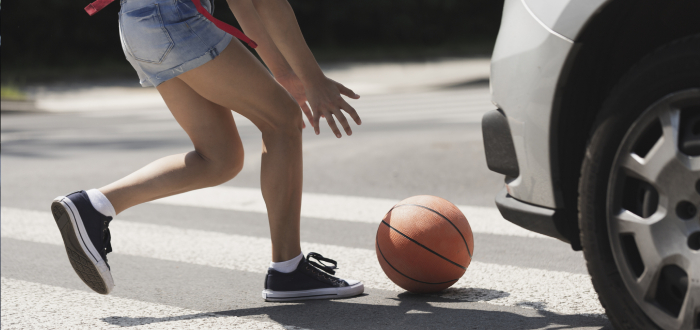 A girl runs into the street to get her ball as a car drives at her