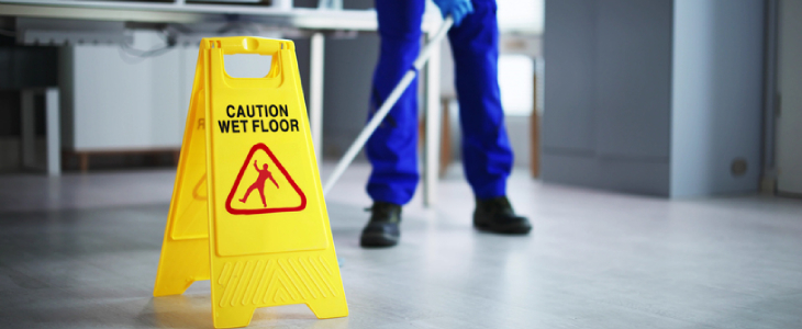 Janitor cleaning the floor with a wet caution floor sign